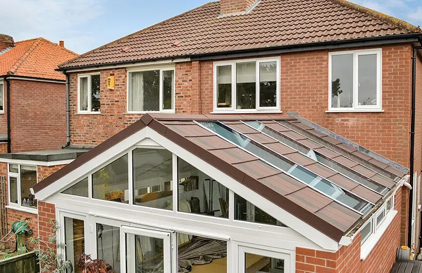 A brick house with a conservatory featuring a brown-tiled roof and glass panels.
