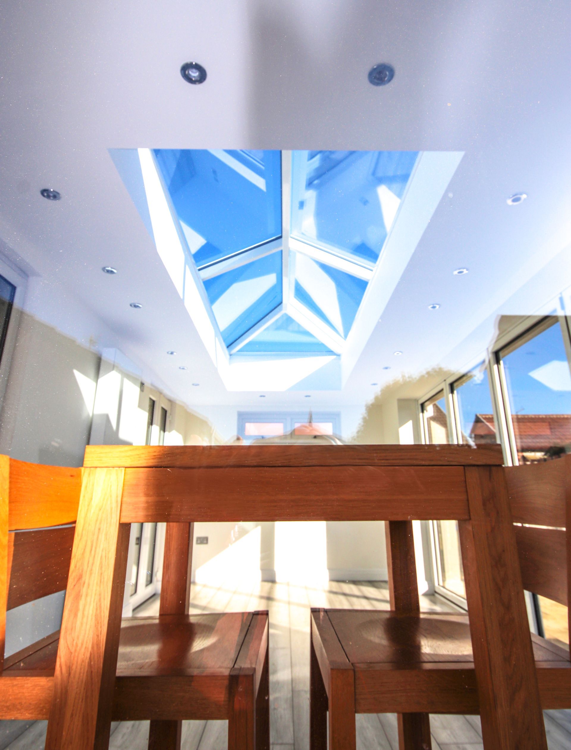 Wooden table and chairs in a light-filled room with a large skylight, bright blue sky visible.