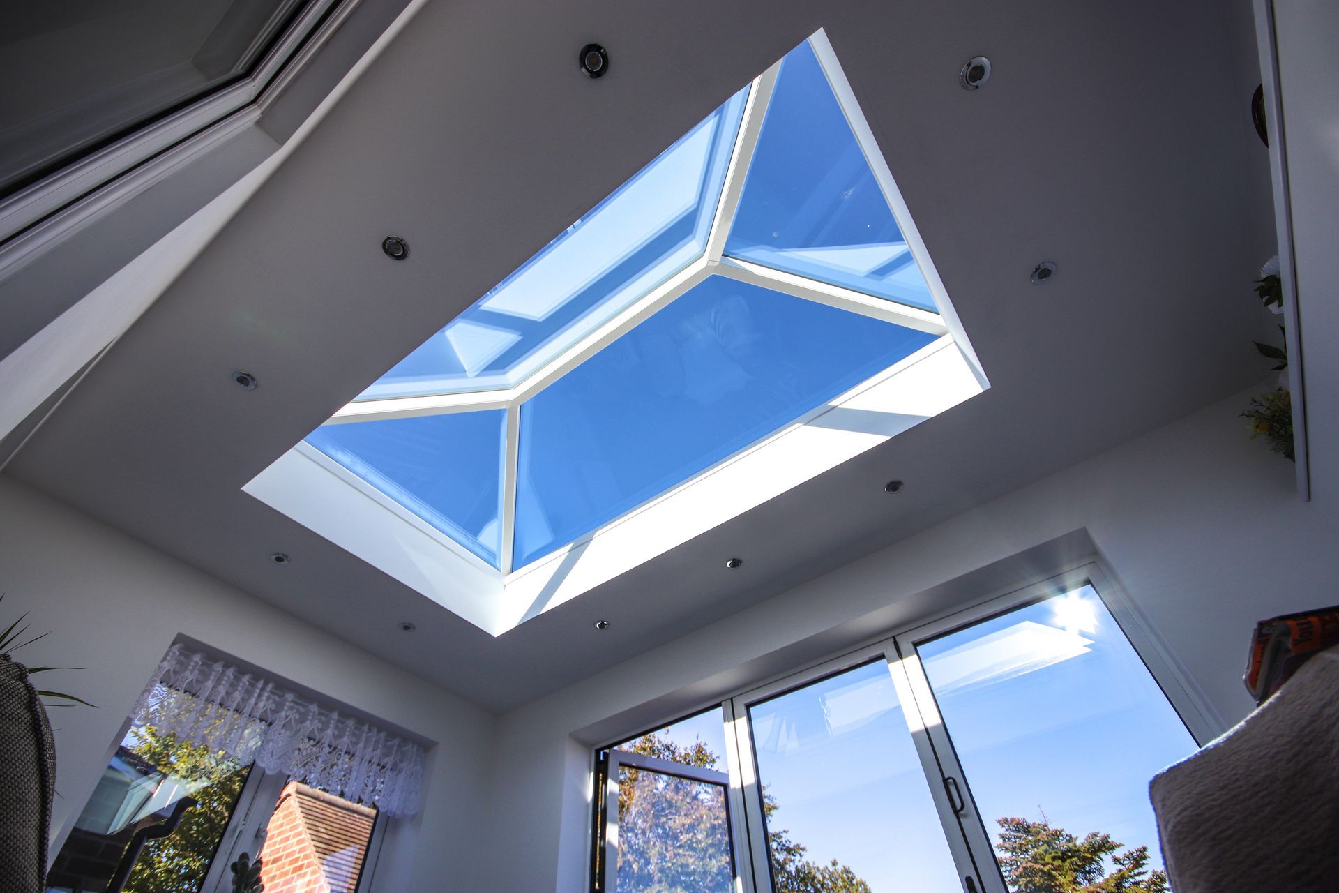 Skylight in a white-walled room with a blue sky visible. Large glass windows and recessed lighting.