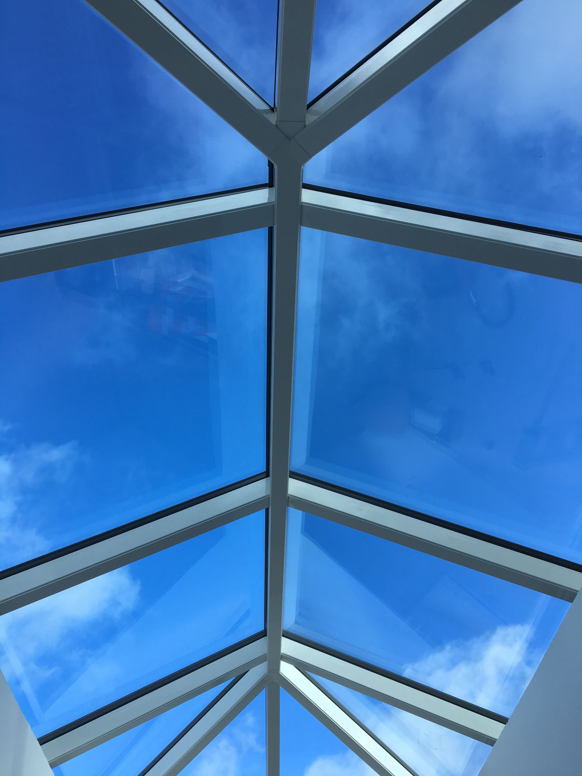Skylight view of bright blue sky with white frame and thin clouds.