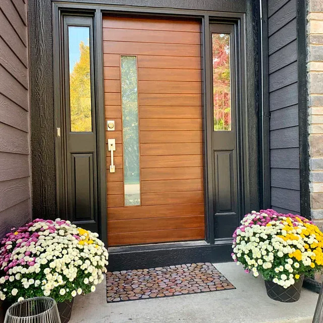 Modern wooden front door with side windows and planters of flowers.