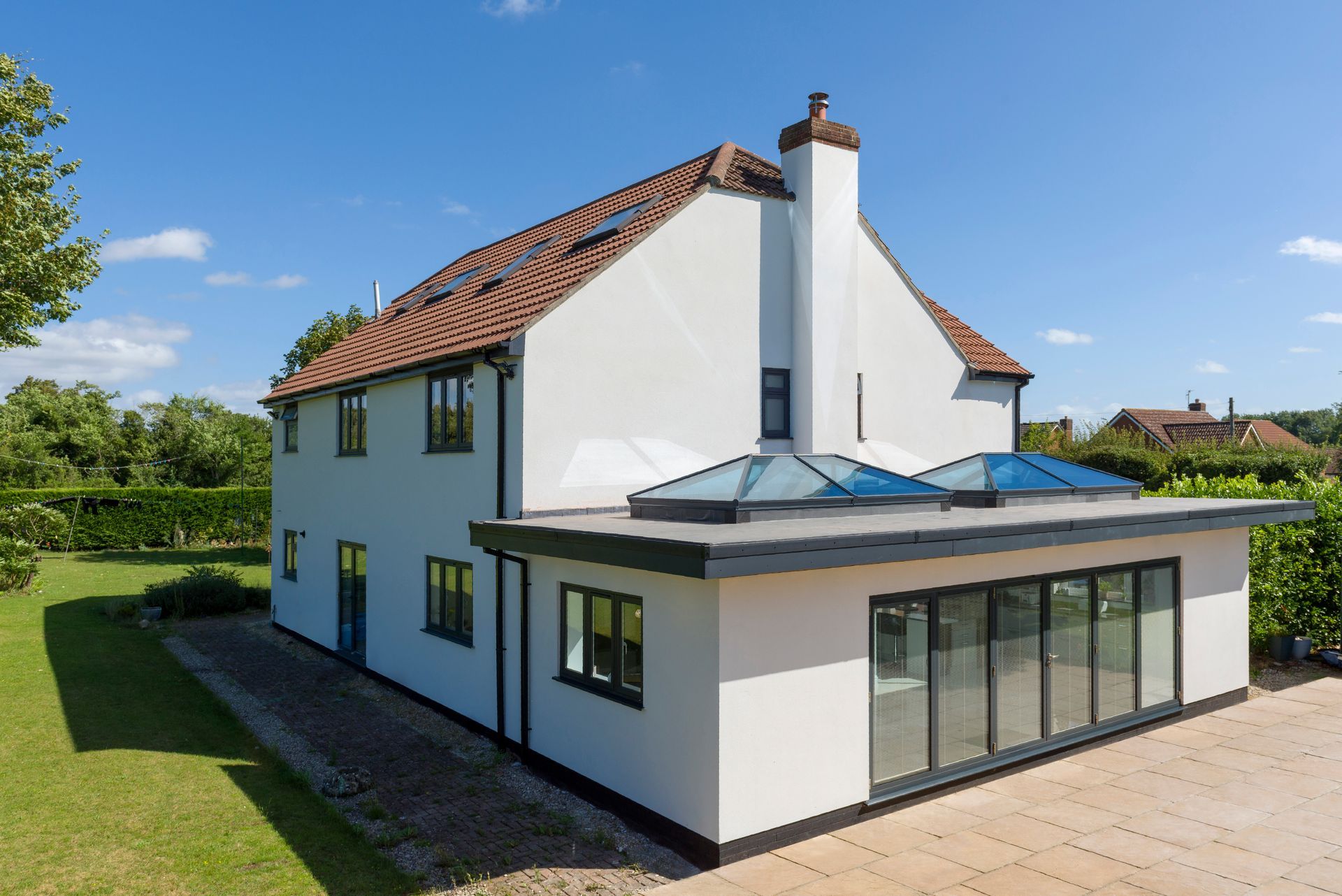 White house with a flat-roofed extension featuring large windows and skylights; a sunny day.