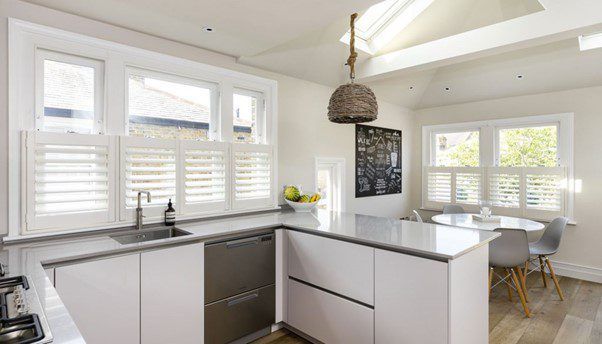 Modern kitchen with white cabinets, stainless steel appliances, shutters, and island.