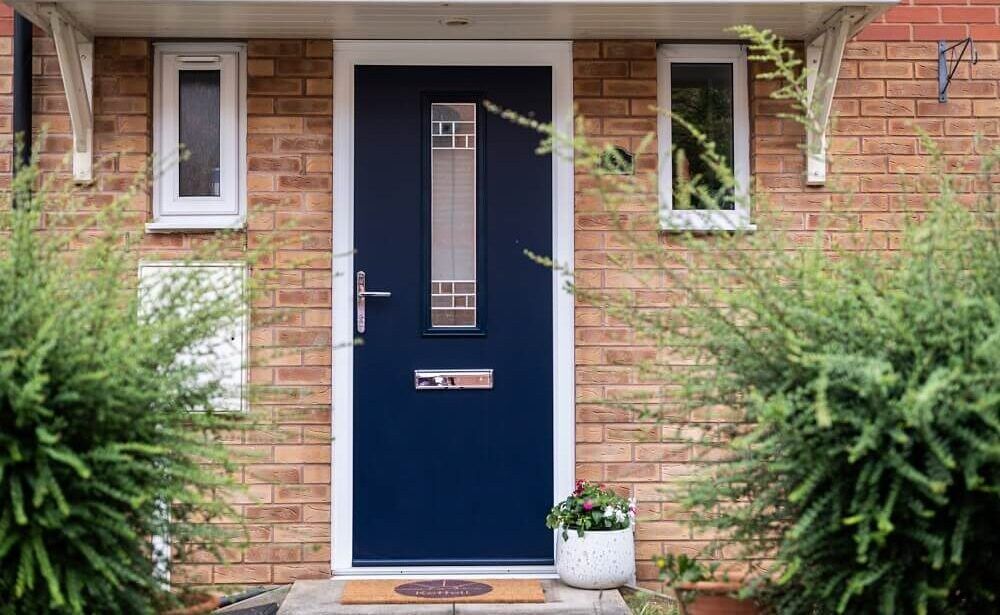 Blue front door with long window, surrounded by small white windows, on a brick building.