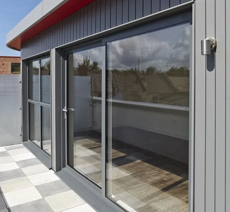 Gray building with large glass doors reflecting sky and trees.