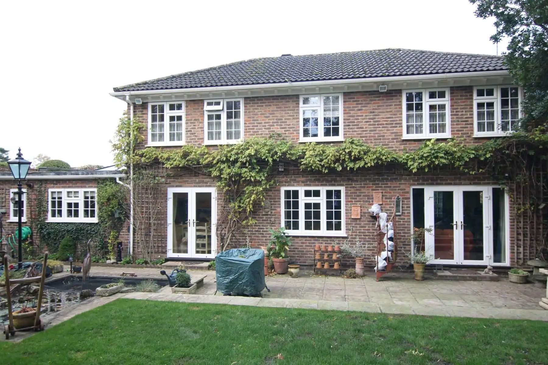 Two-story brick house with white-framed windows and doors, green vines, patio, and lawn.