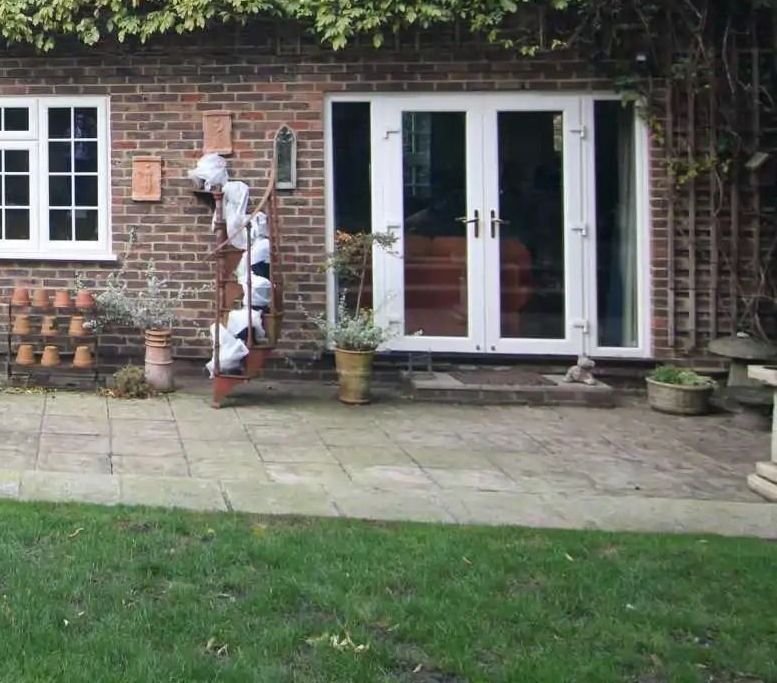 Brick building with white-framed double doors and window, stone patio, green lawn, and decorative metal sculpture.