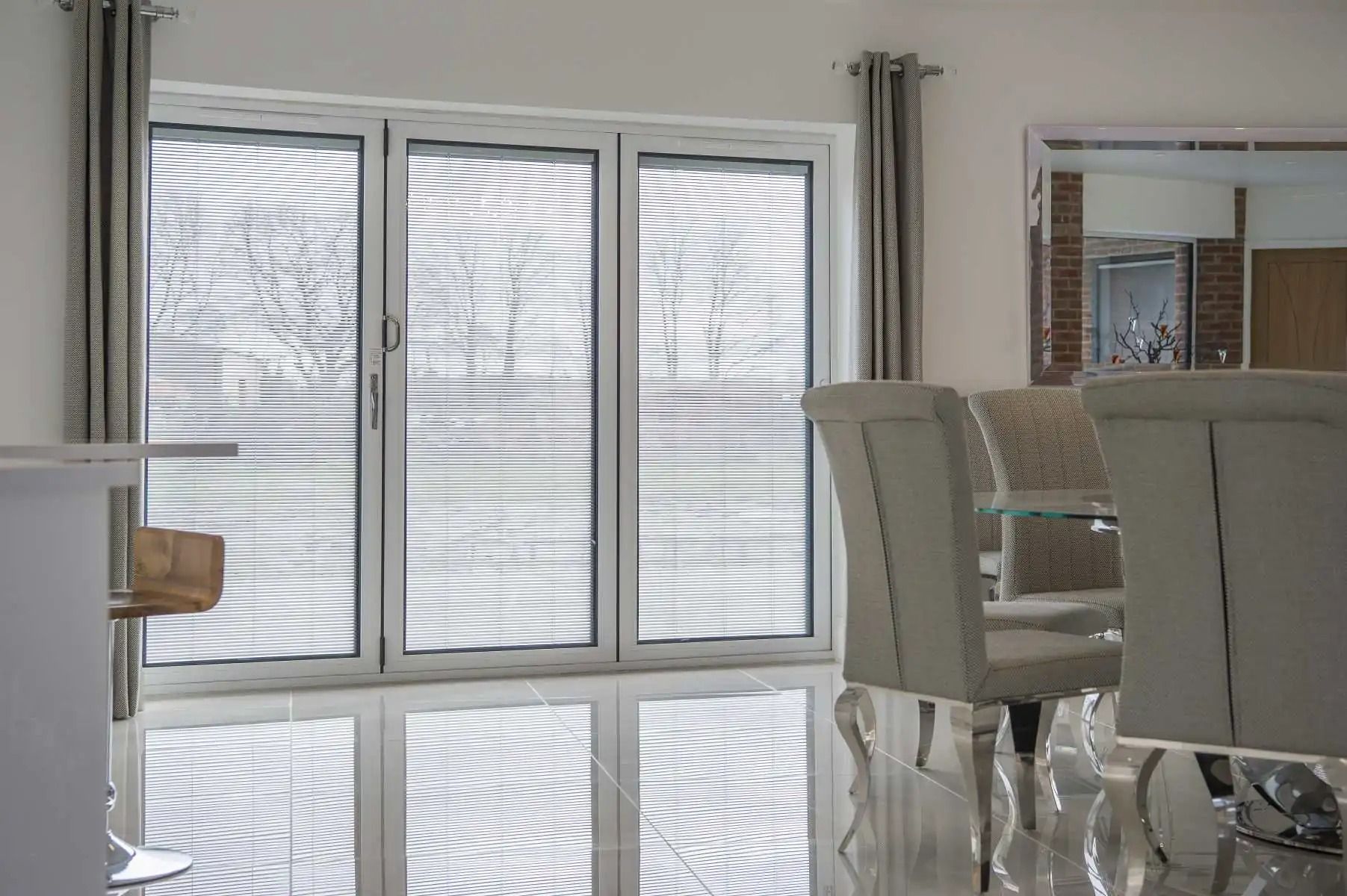 A modern dining room with a table and chairs, a large window, and reflective flooring.