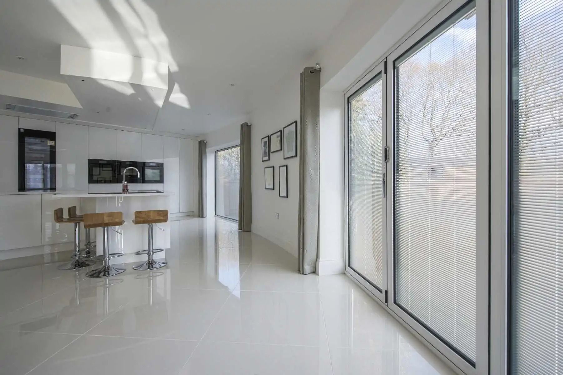 Bright, modern interior with glossy white floors, kitchen, bar stools, and textured glass doors.
