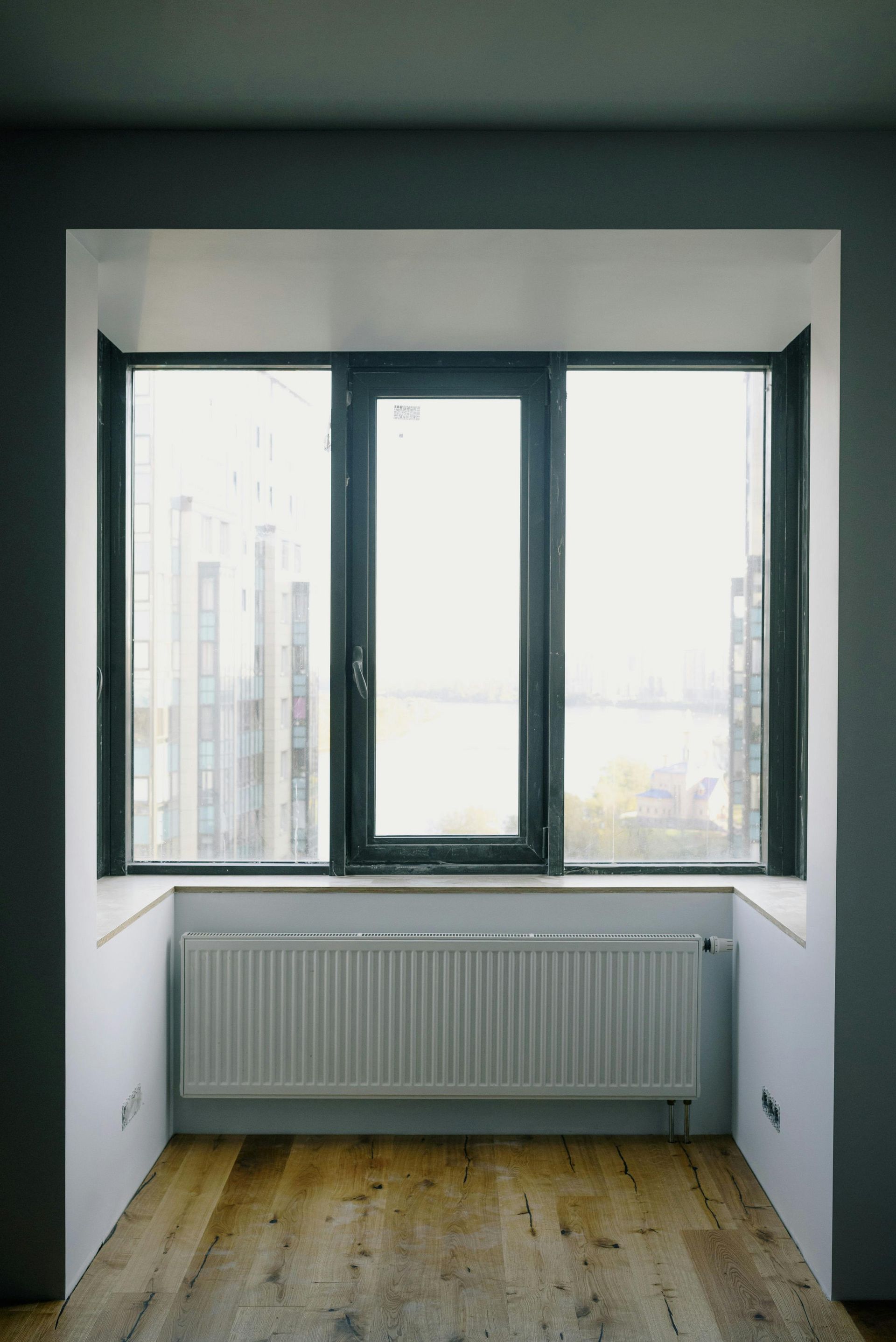 Window nook with a white radiator, hardwood floor, and a view of a cityscape.