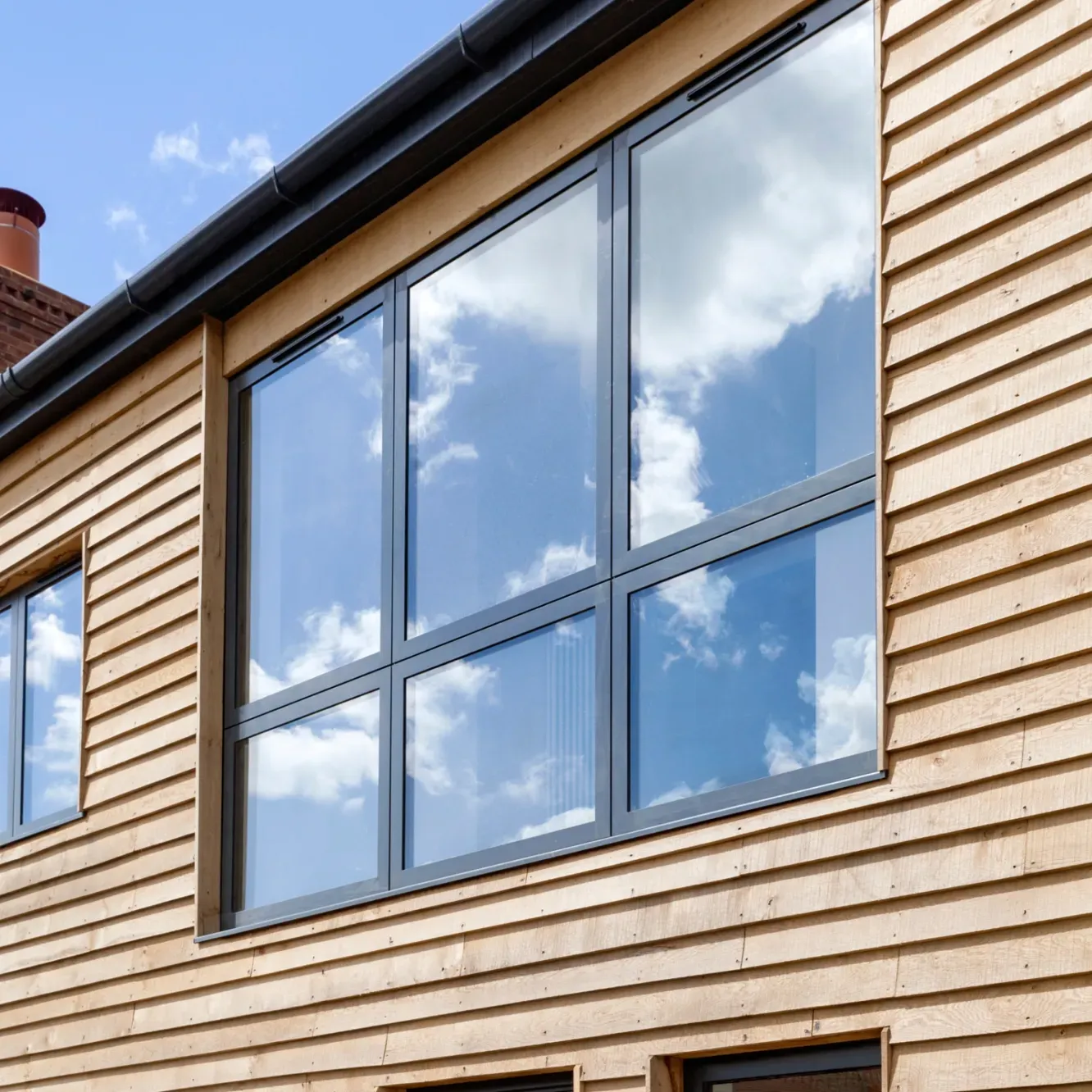Large multi-pane window reflecting a cloudy blue sky, set in a wooden wall.