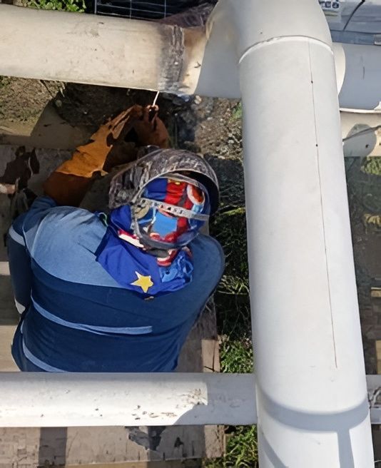 Tres técnicos con monos azules y cascos blancos trabajan en tuberías industriales en una planta.