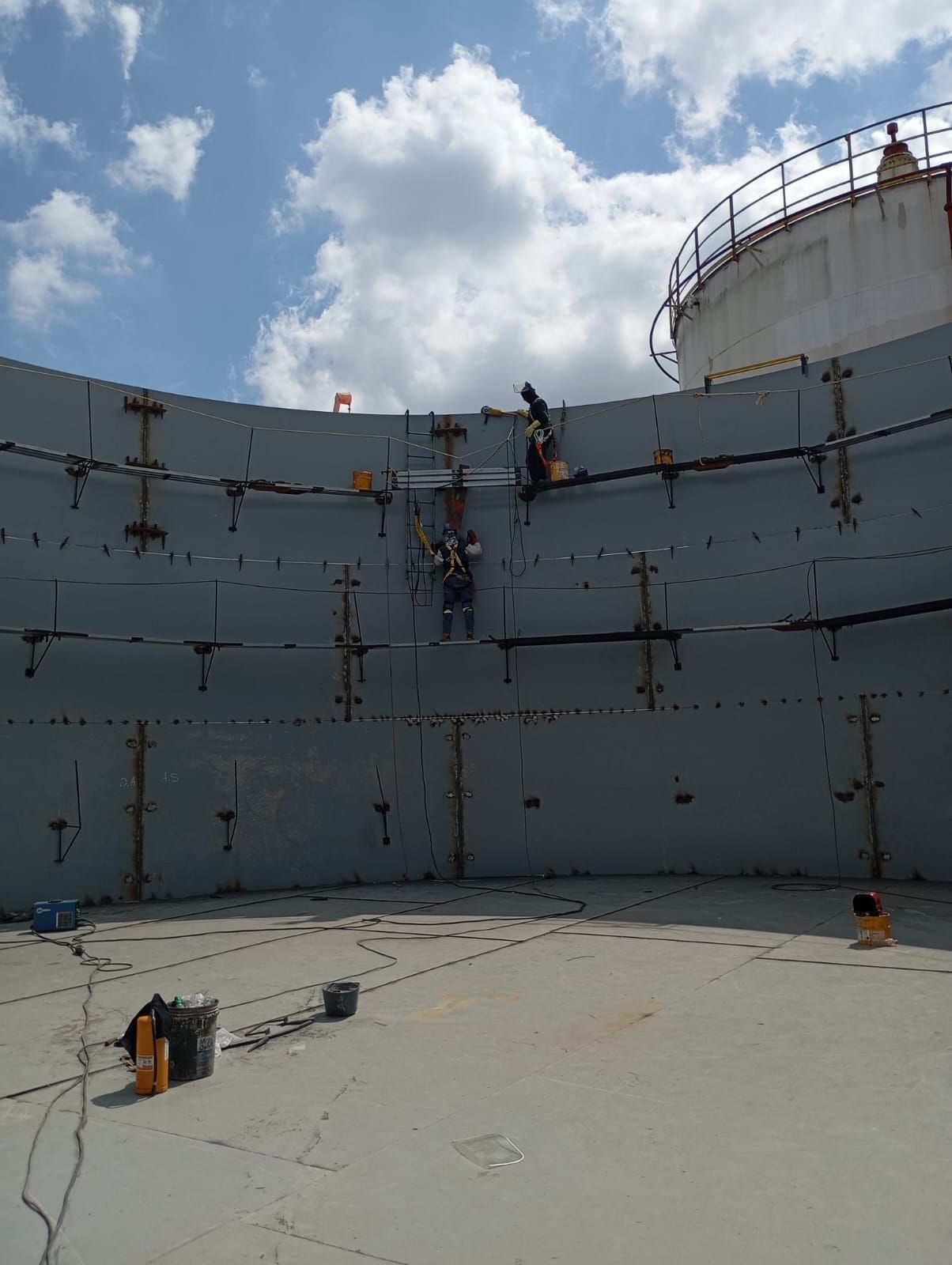 Una apisonadora compacta la tierra cerca de grandes tanques de almacenamiento blancos en un emplazamiento industrial.