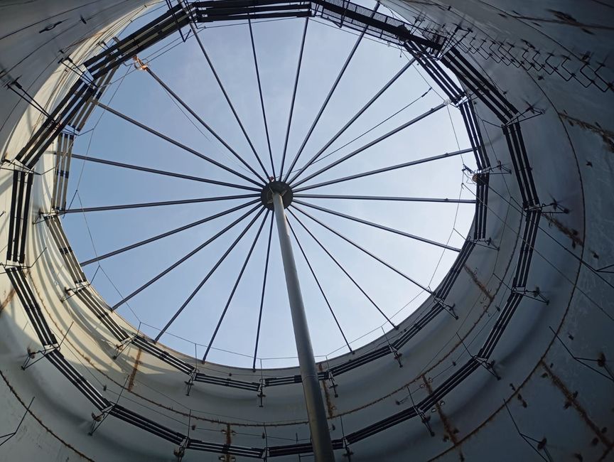 Vista interior de una cúpula circular con tragaluz y soportes metálicos radiales contra un cielo azul.