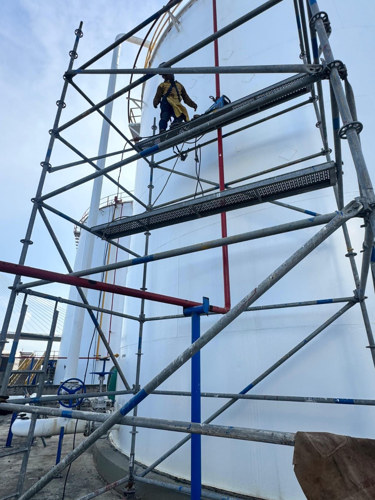 Un trabajador se encuentra en un andamio a gran altura, con un arnés de seguridad, cerca de un edificio en construcción.