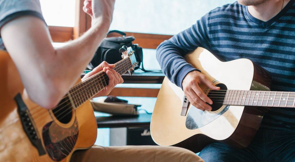 Two people playing guitars in a casual setting.
