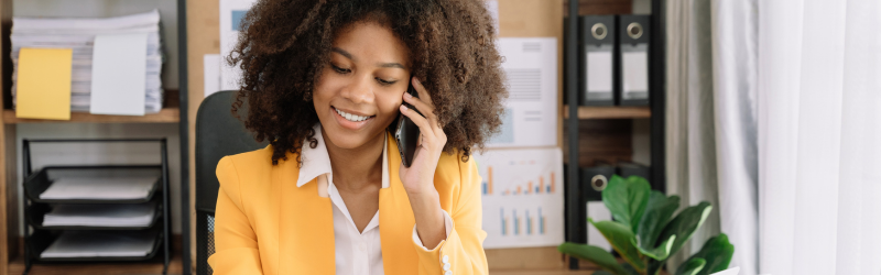 A woman is sitting at a desk talking on a cell phone.