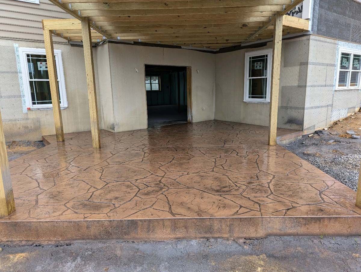 A concrete patio with a wooden pergola over it in front of a house under construction.