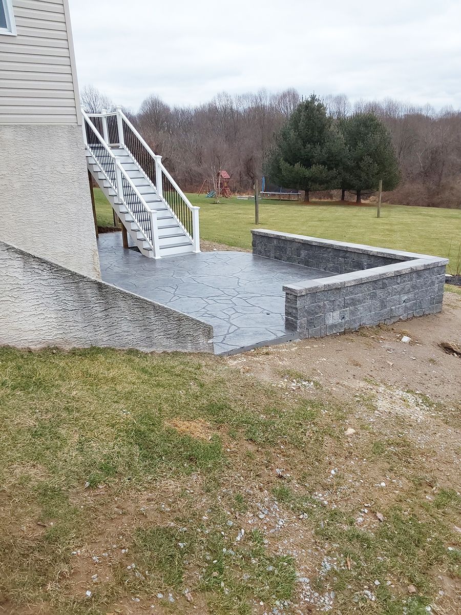 A concrete patio with stairs leading up to it is in the backyard of a house.