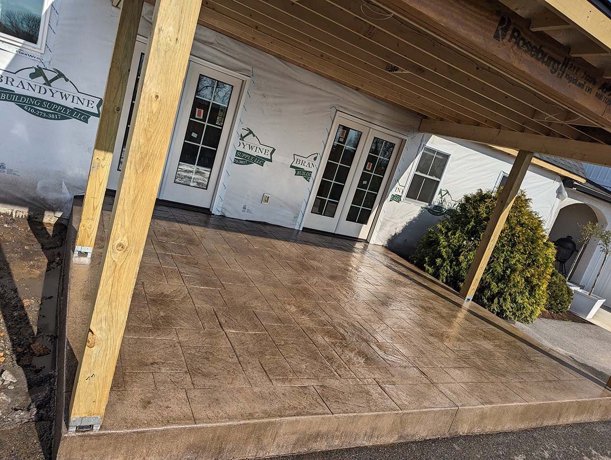 A patio with a wooden roof and a white house in the background.