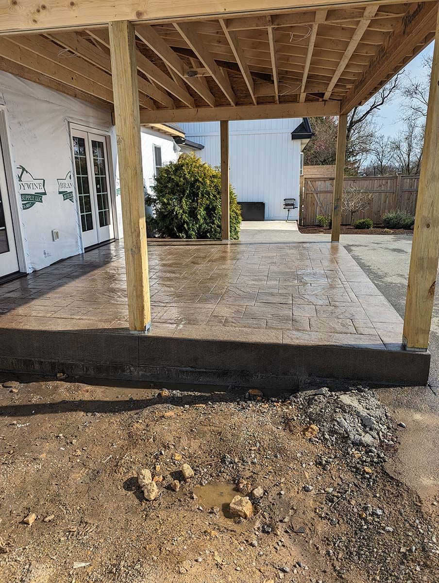 A concrete patio under a wooden structure in front of a house.