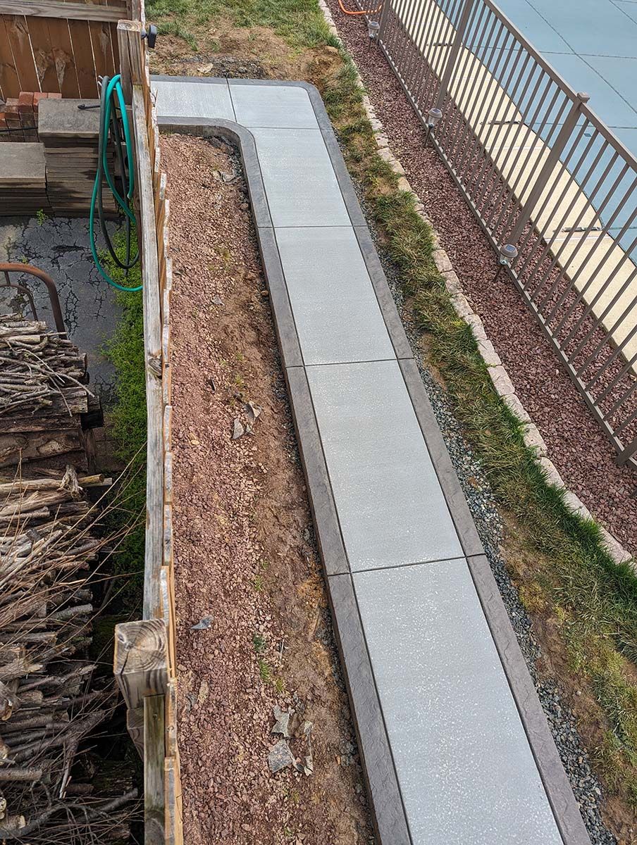 A concrete walkway is being built next to a fence.