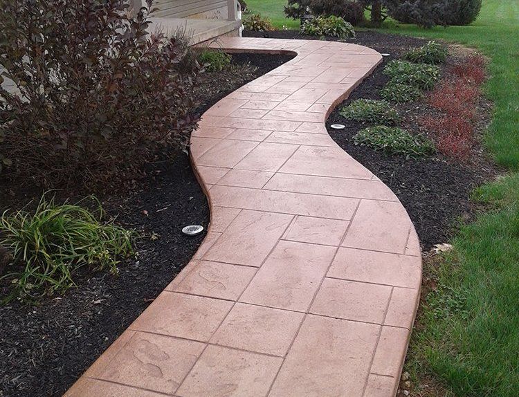 A concrete walkway going through a lush green yard