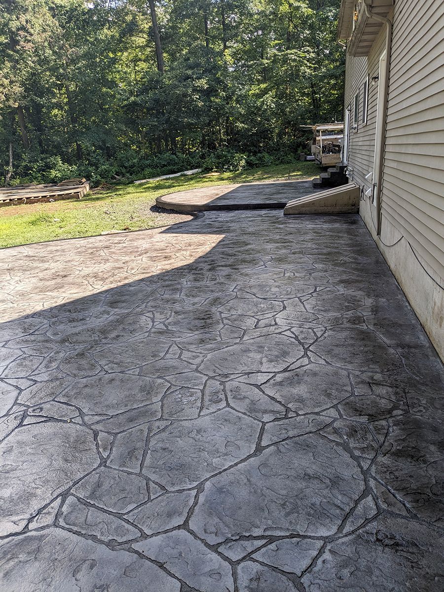 A concrete walkway leading to a house with trees in the background.