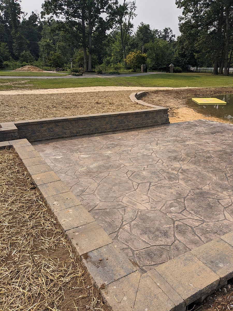 A concrete patio with a stone wall and a pond in the background.