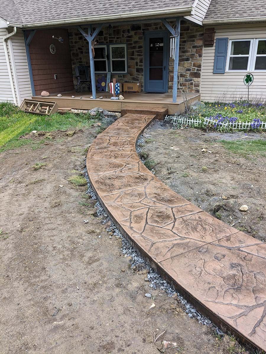 A concrete walkway leading to a house with a porch.