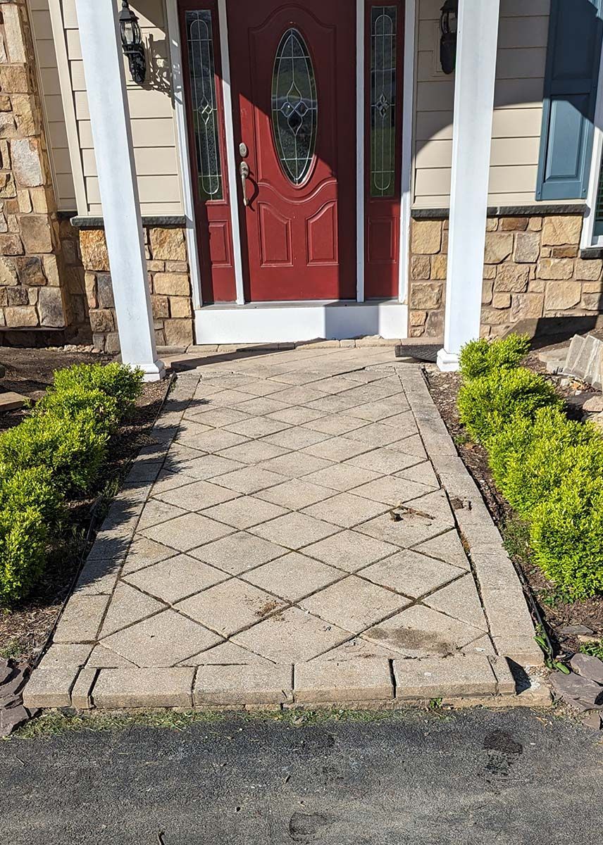 A brick walkway leading to a red door of a house.