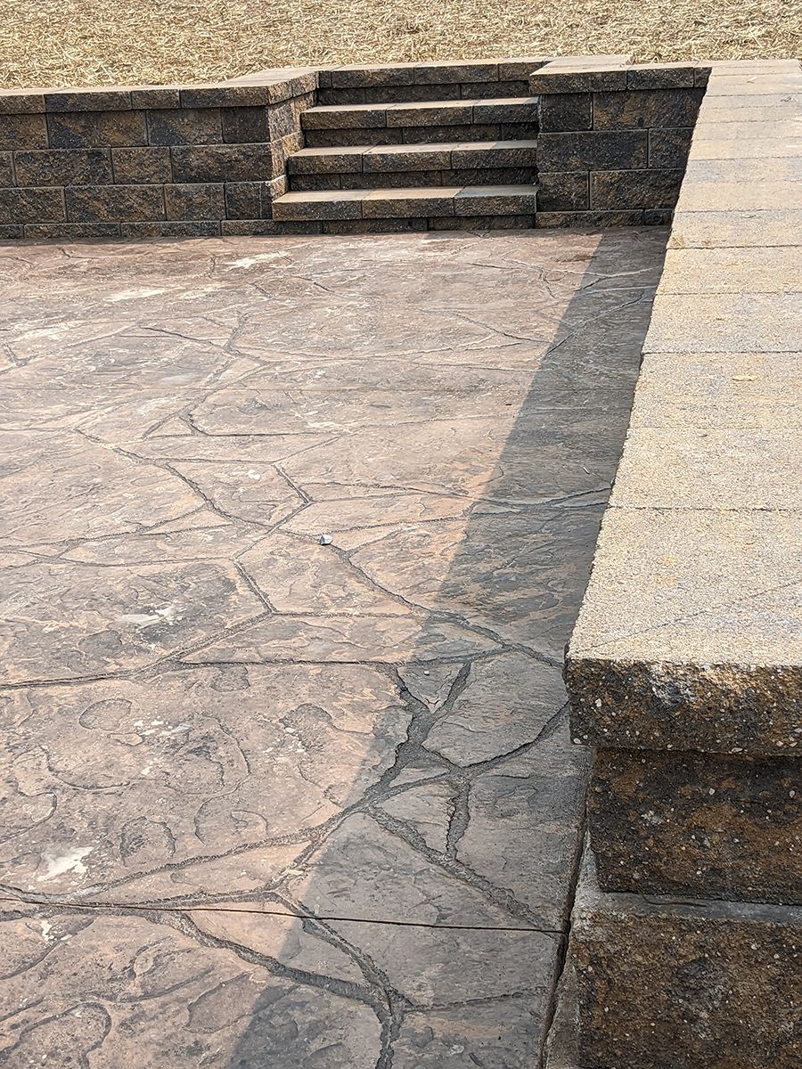 A concrete patio with stairs and a stone wall.