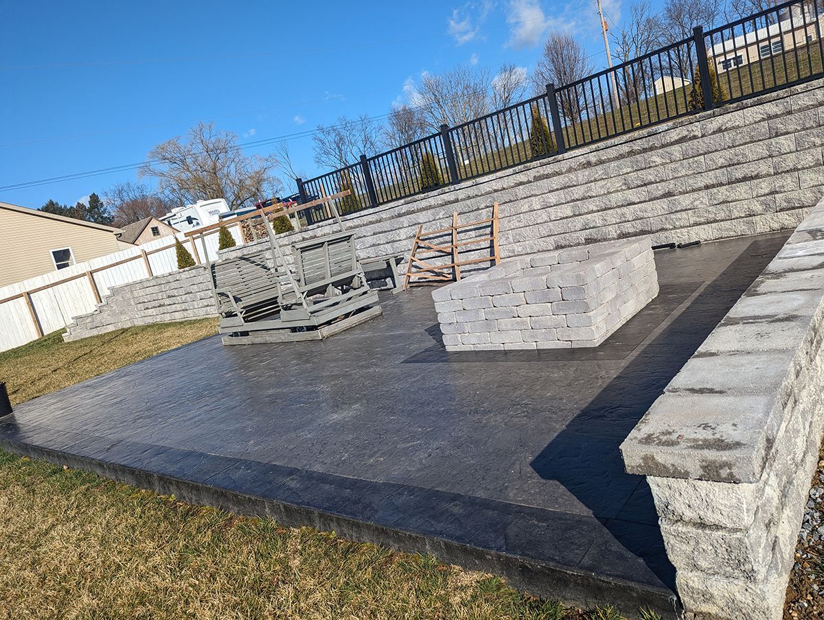 A concrete patio with a fire pit and a fence in the background.