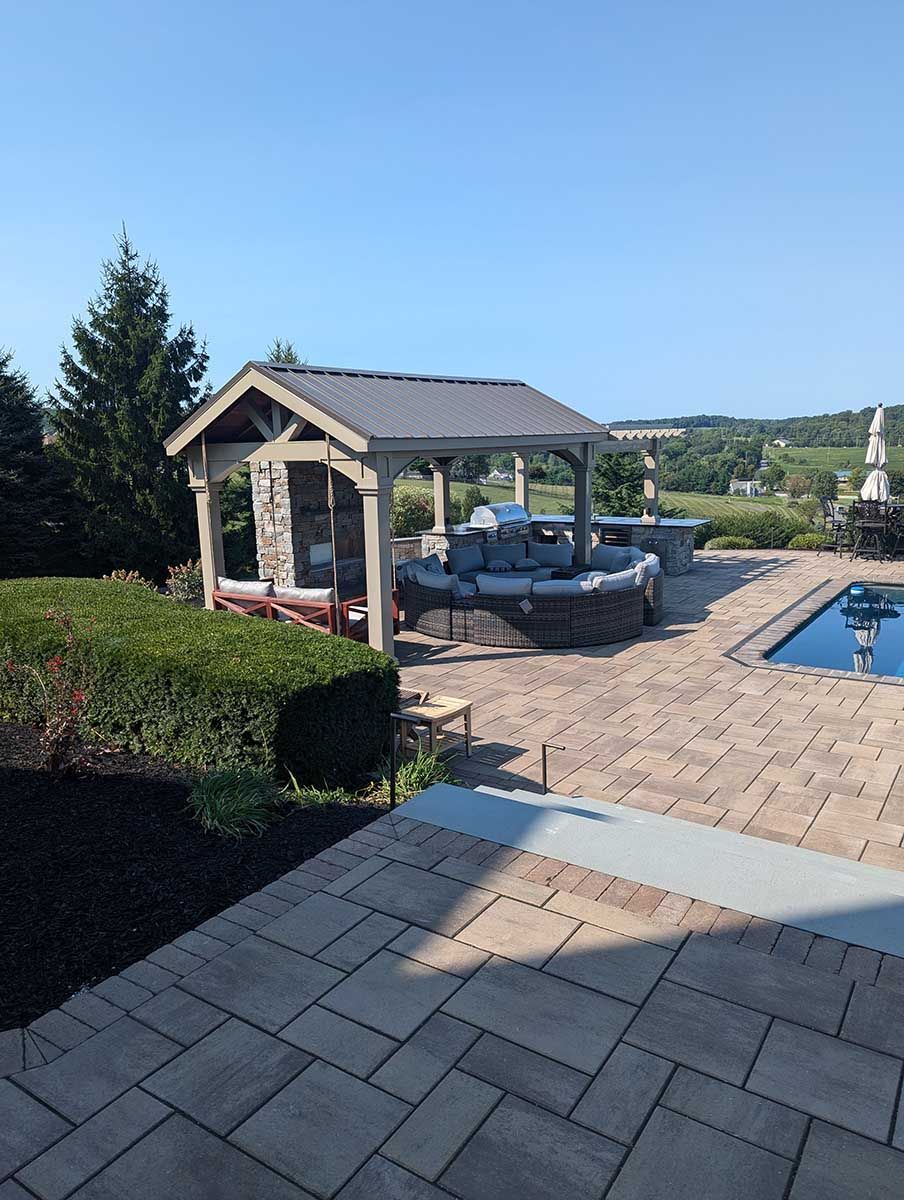 A patio with a gazebo and a pool in the background