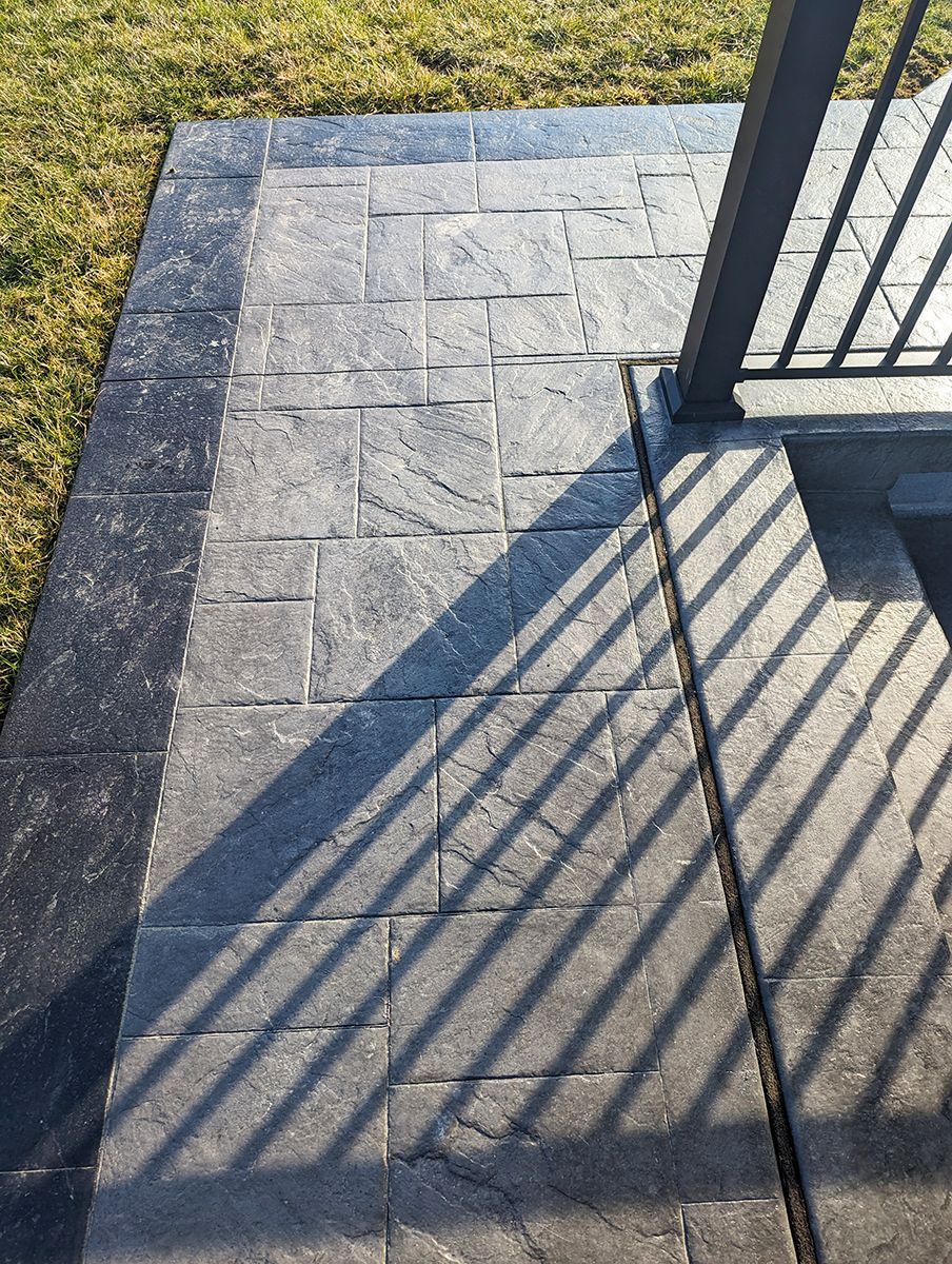 A shadow of a fence is cast on a brick walkway.