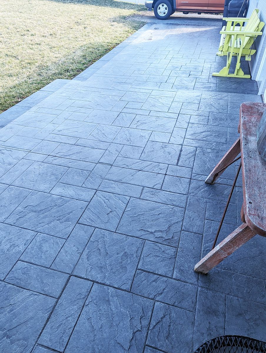 A concrete patio with a bench and chairs on it.