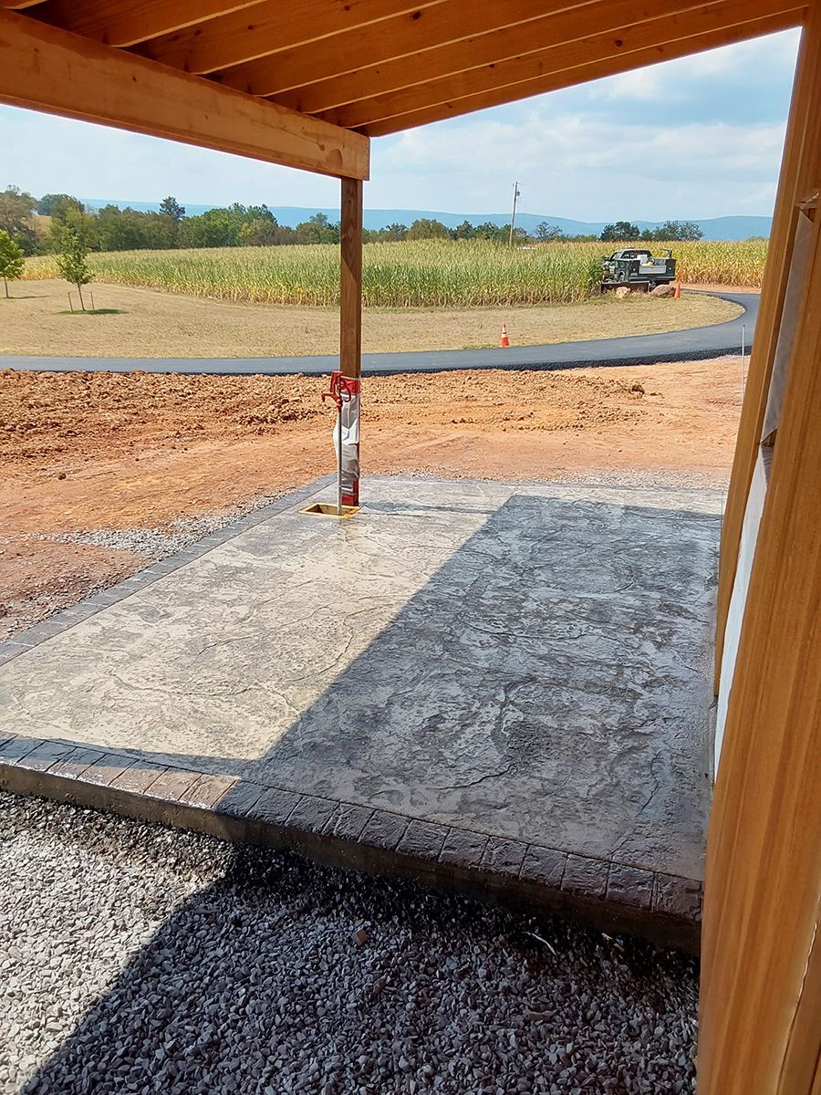 A concrete walkway under a wooden roof with a view of a field.