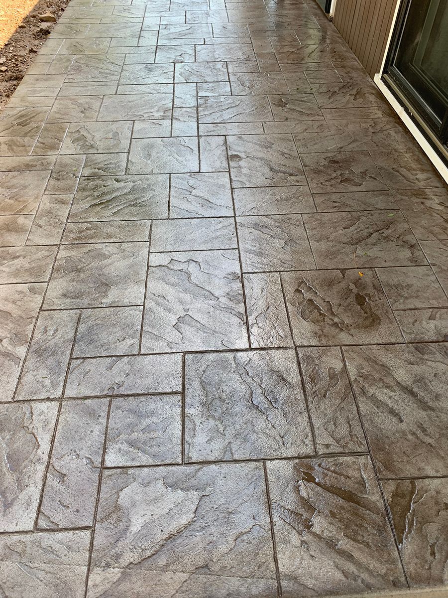 A concrete walkway with a brick pattern and a sliding glass door.