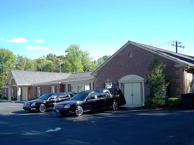 Two black hearses parked outside a brick building, possibly a funeral home, on a sunny day.