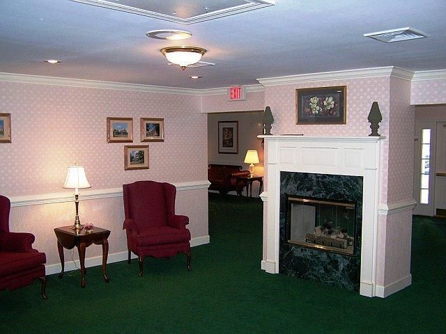 Interior waiting area with fireplace, red armchairs, green carpet, and pink wallpaper.
