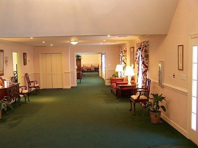 Long hallway in a building with green carpet, pink walls, furniture, and plants; doors on the right.