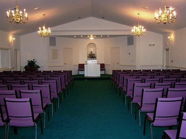Interior of a chapel with purple chairs, chandeliers, and a central podium.