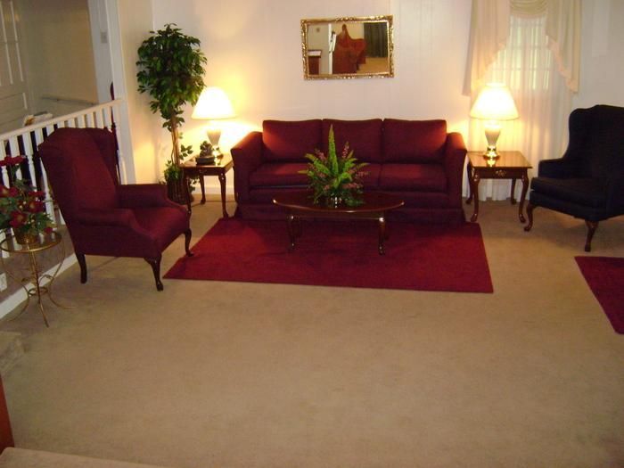 Living room with maroon sofa, chairs, and rug; neutral walls and floor.