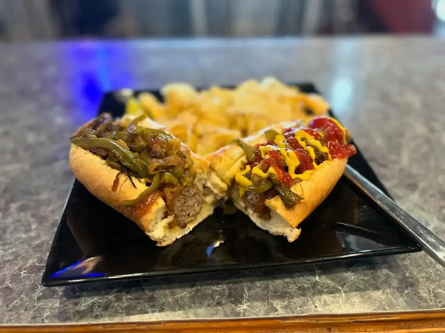 A hot dog and french fries on a black plate on a table.