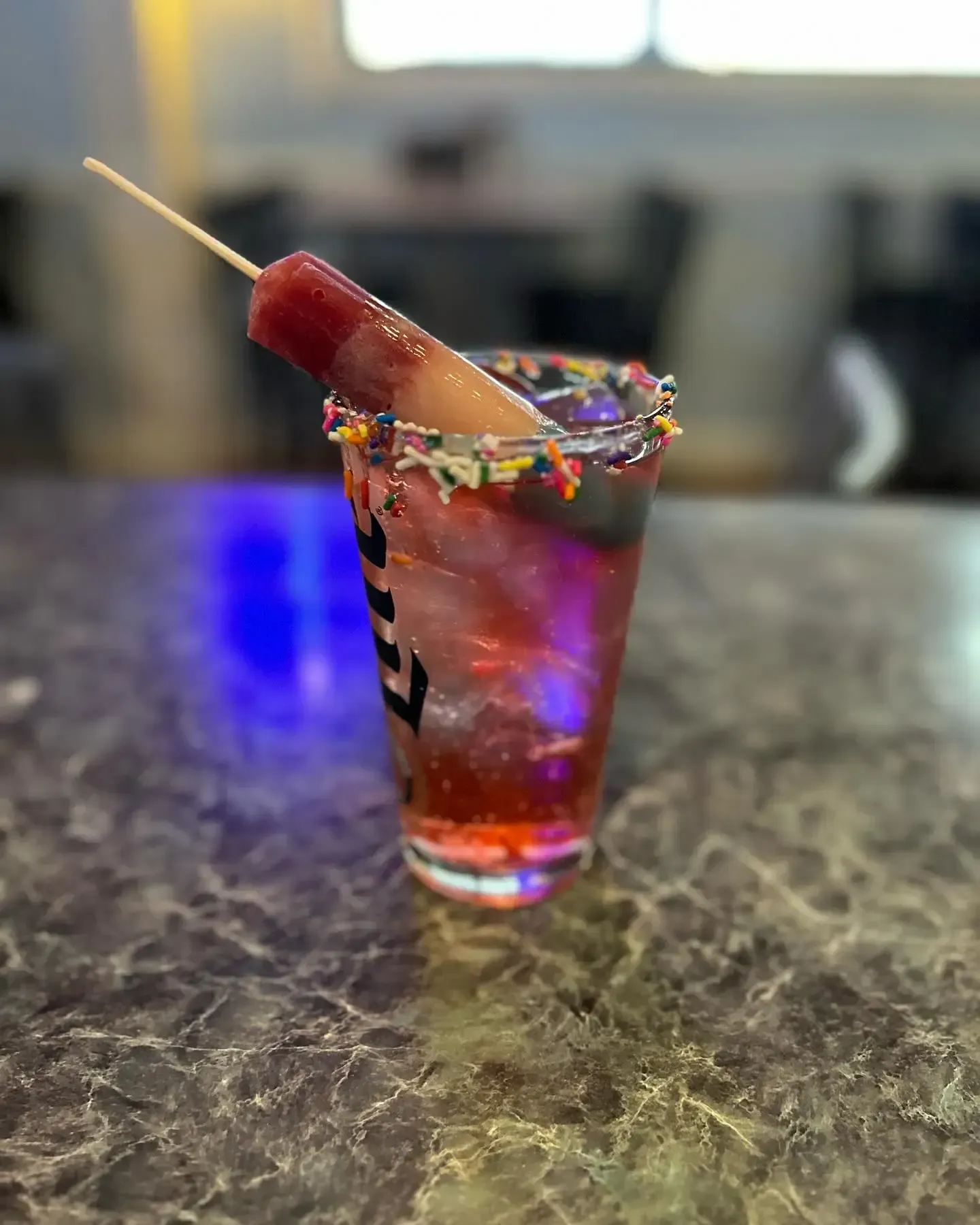 A shot glass filled with a drink and a popsicle on a stick.