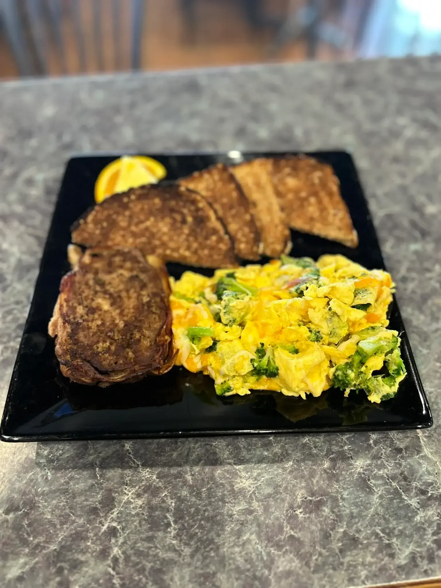 A plate of food with meat , eggs , broccoli and toast on a table.
