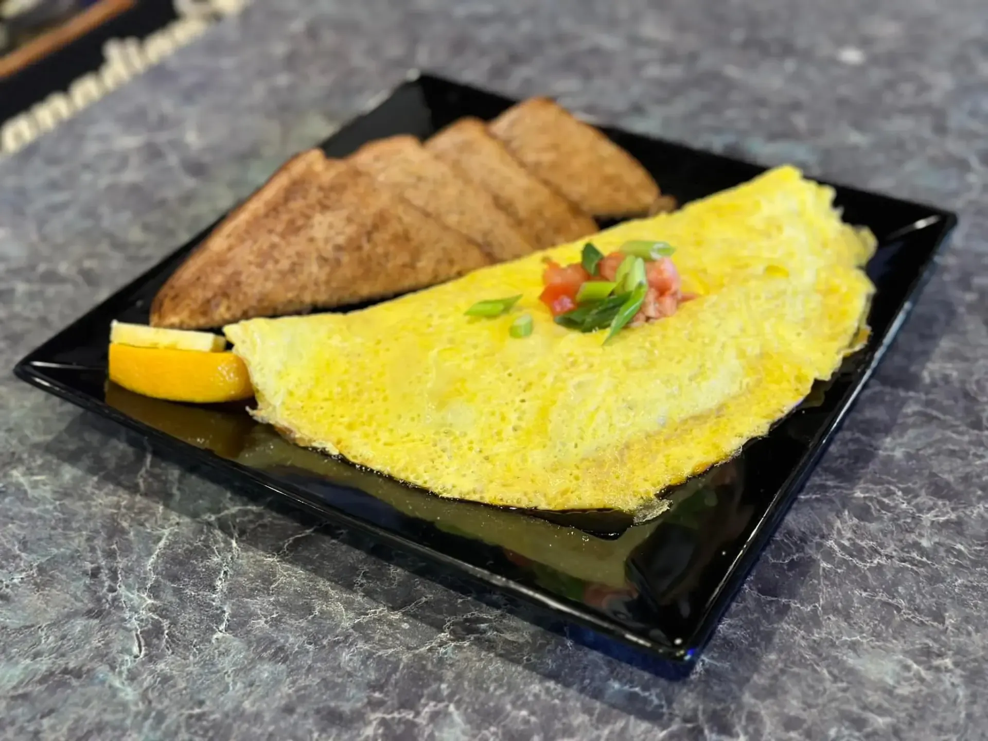 A plate of food with an omelet and toast on a table.