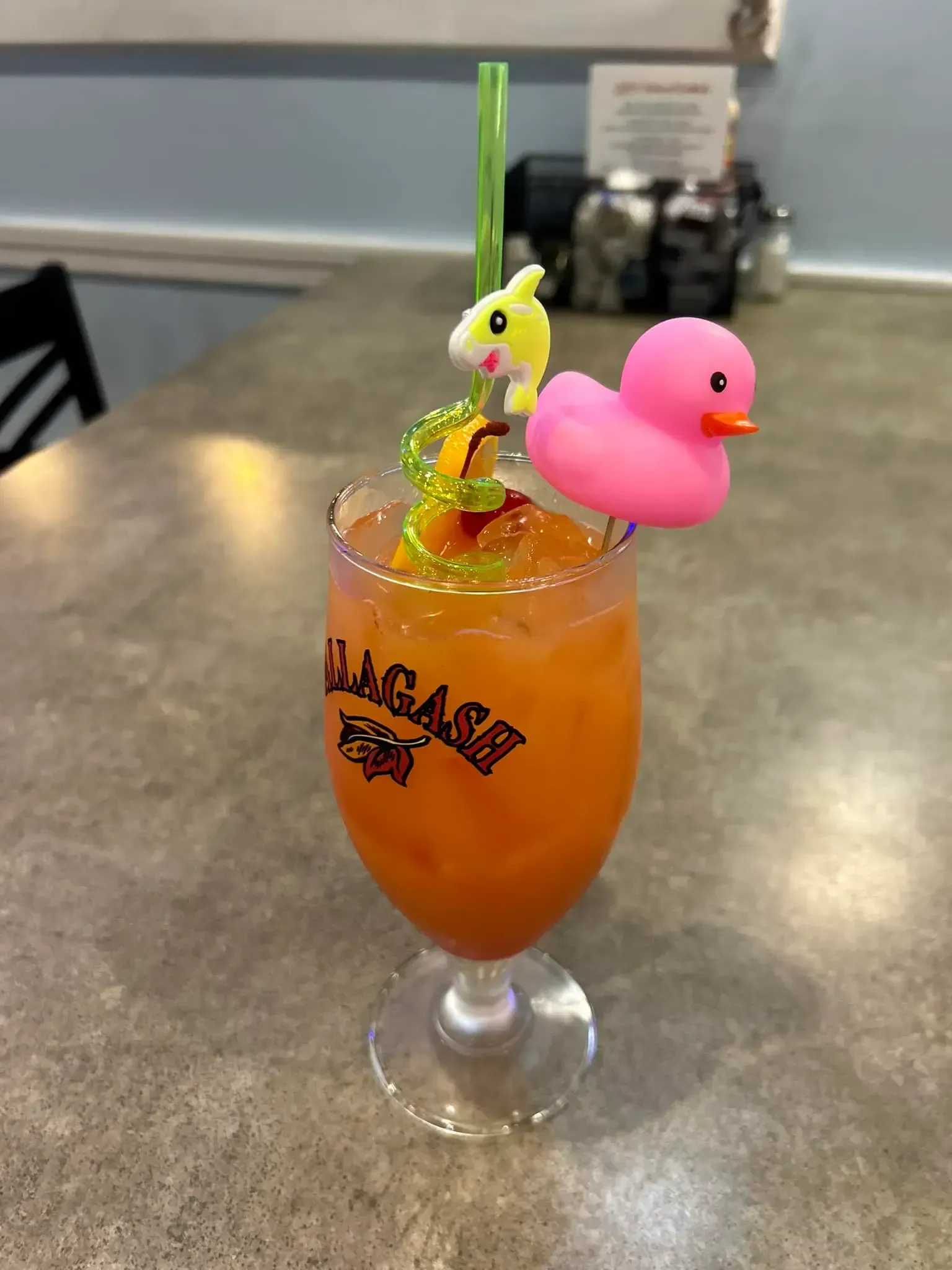 A glass of orange juice with a pink rubber duck on top of it.