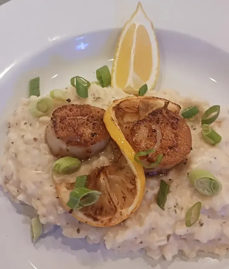 A close up of a plate of food with scallops and lemon slices