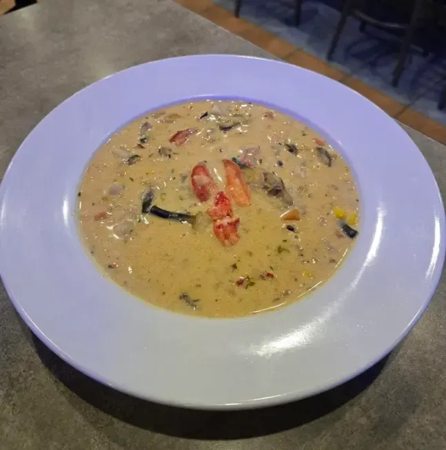 A bowl of soup with tomatoes and corn on a table.